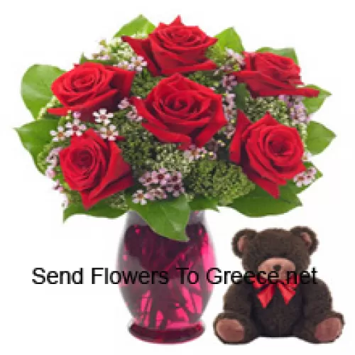 שבע ורדים אדומים עם כמה עלי פרנים בצנצנת זכוכית יחד עם דובי גיל 14 אינץ' מקסים