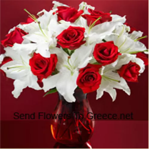 Punaiset ruusut ja valkoiset liljat muutamilla saniaisilla lasimaljakossa