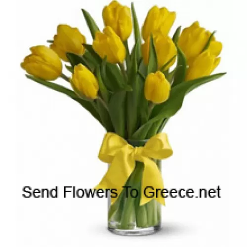 Żółte tulipany z dodatkiem sezonowych wypełniaczy i liści w szklanej wazie - Prosimy zauważyć, że w przypadku braku określonych kwiatów sezonowych zostaną one zastąpione innymi kwiatami o tej samej wartości