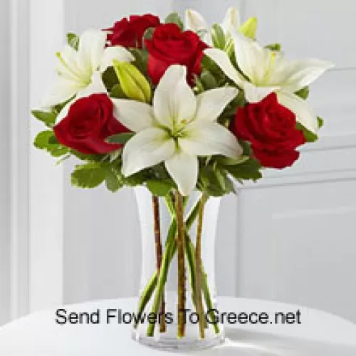 Punaisia ruusuja ja valkoisia liljoja muutamilla sesongin täytteillä lasimaljakossa