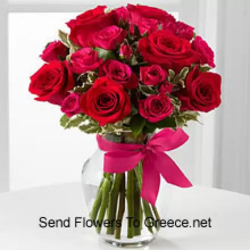19 красных роз с сезонными наполнителями в стеклянной вазе, украшенной розовым бантом
